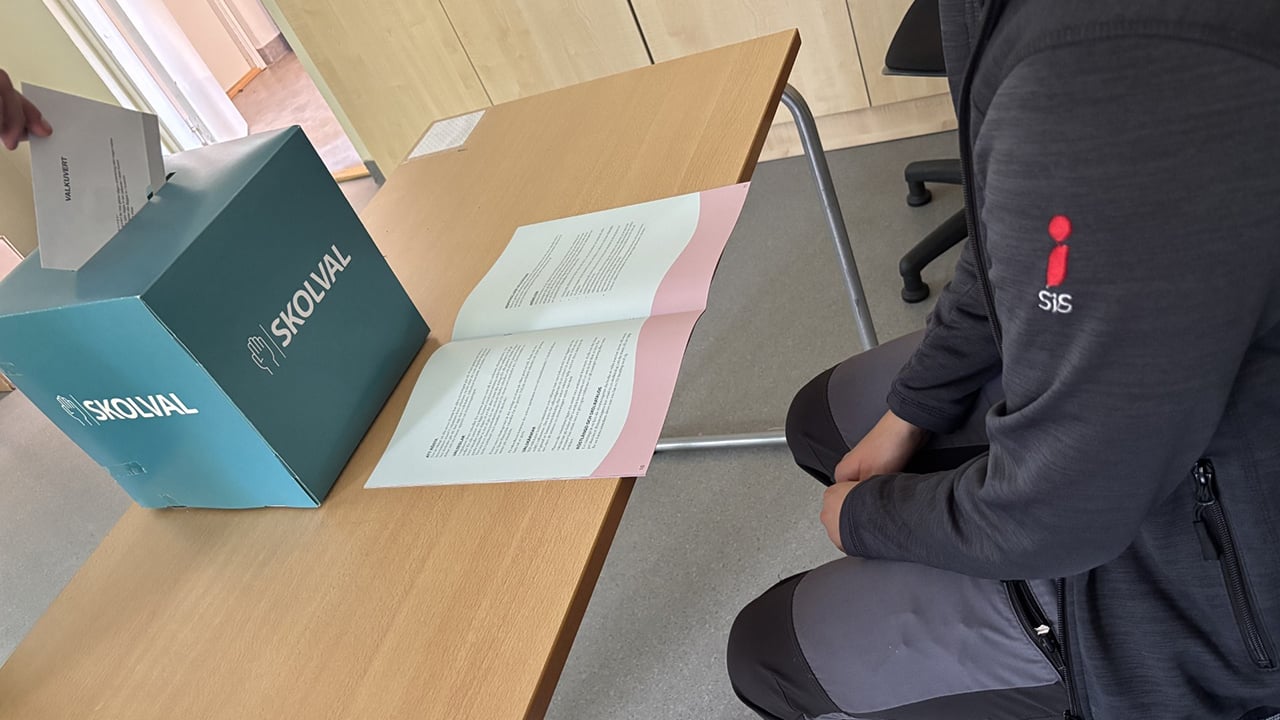 En röstsedel läggs i en valurna under överseende av en SiS-anställd