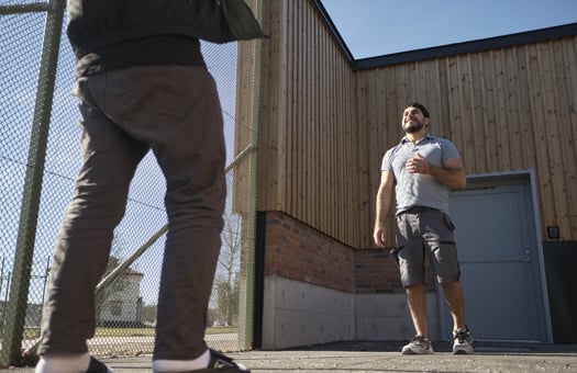 Medarbetare och ungdom står mittemot varandra på en inhägnad utomhusgård under en fritidsaktivitet.