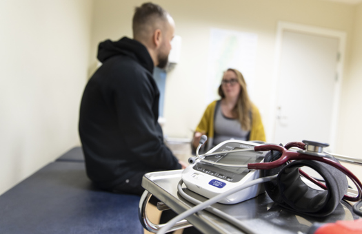 En manlig patient sitter på en behandlingsbrits och pratar med en sjuksköterska.