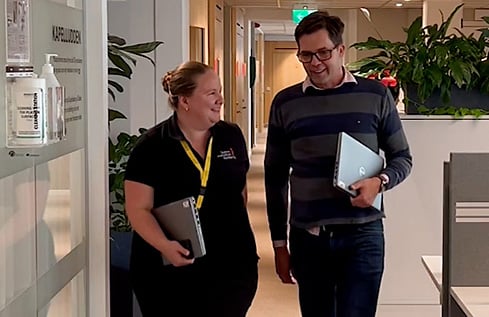 Två medarbetare som samtalar och går bredvid varandra i ett kontorslandskap. 