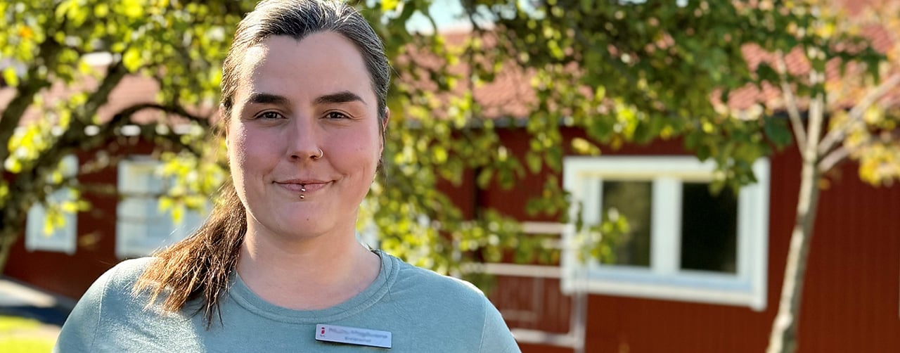 Närbild på Maggie en solig sommardag med ett rött hus i bakgrunden. 