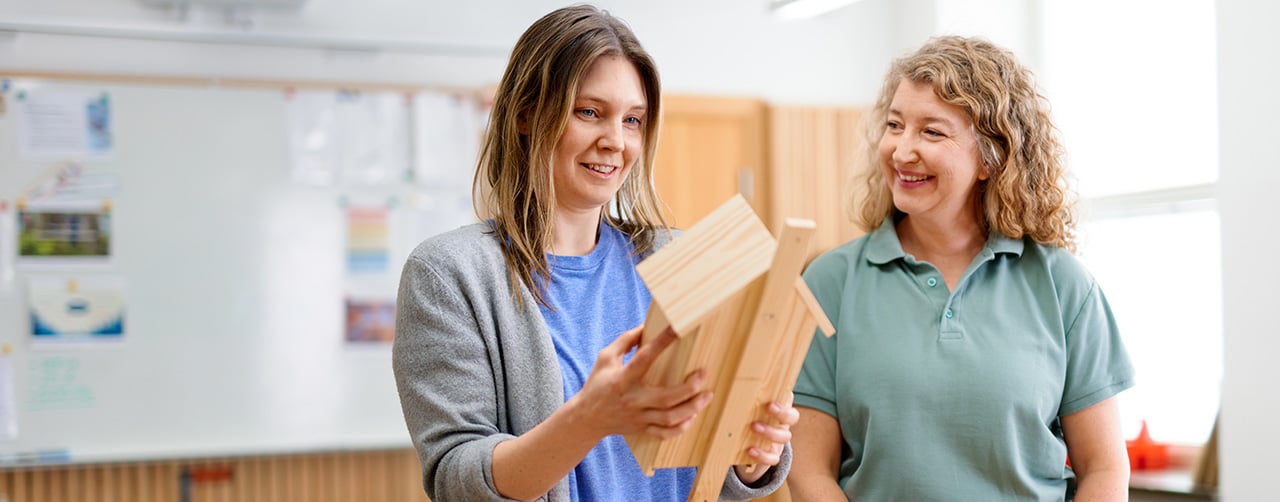 En kvinna i en trädslöjdssal som håller i en fågelholk tillsammans med en behandlingspedagog.