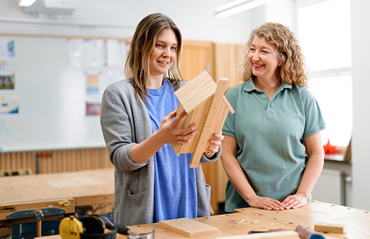 En kvinna i en trädslöjdssal som håller i en fågelholk tillsammans med en behandlingspedagog.