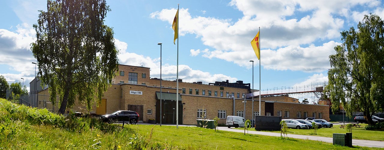 bilden visar en gulbeige byggnad med en parkering framför sig.