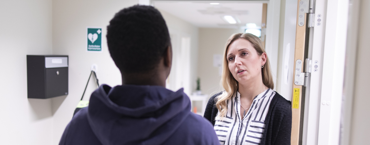Två personer står i en korridor och har ett samtal.