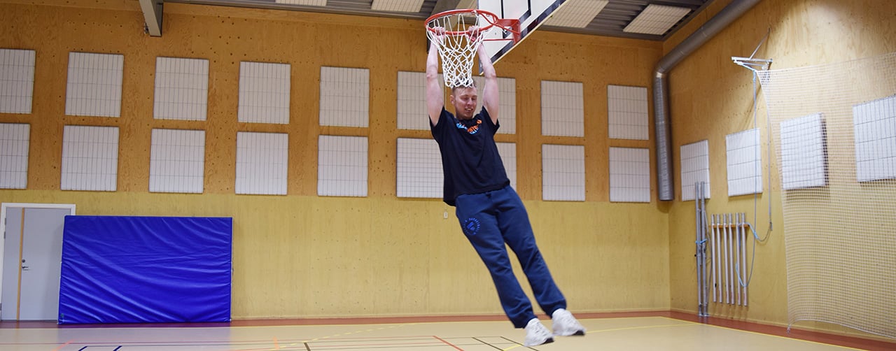 Basketproffset Erik Nilsson visar upp en "slam dunk" (fullträff) i en idrottshall.
